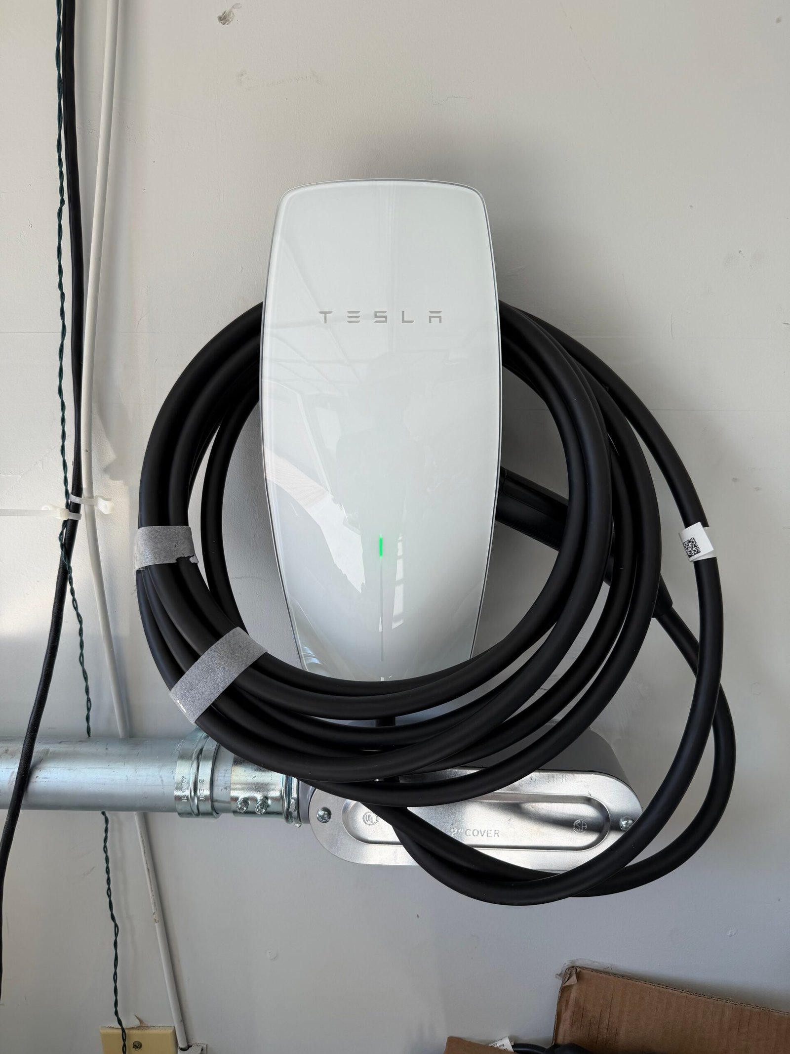 Tesla EV wall connector installed in a garage with coiled charging cable