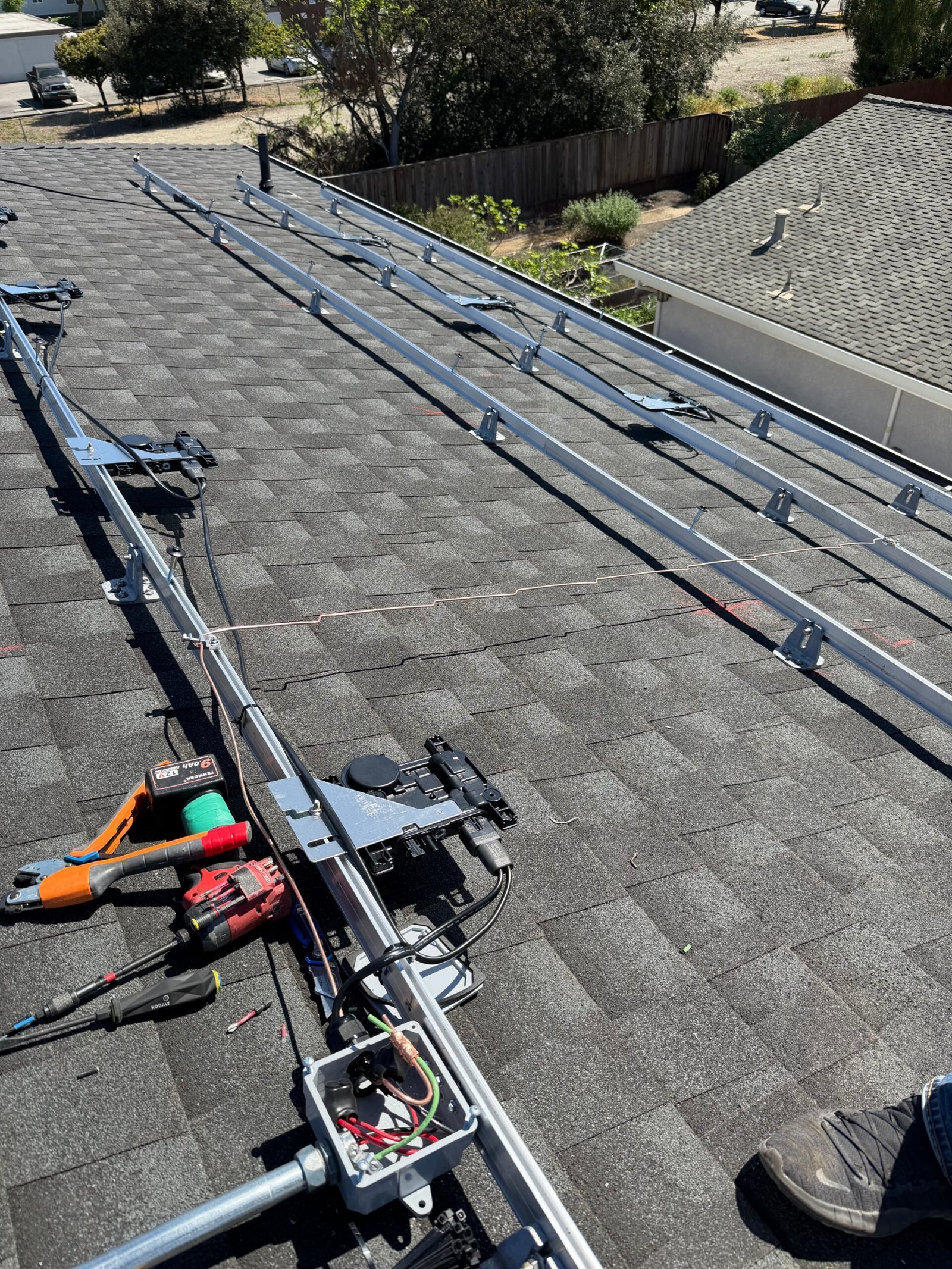 Solar panel racking rails installed on a shingle roof, mid-installation, with tools visible