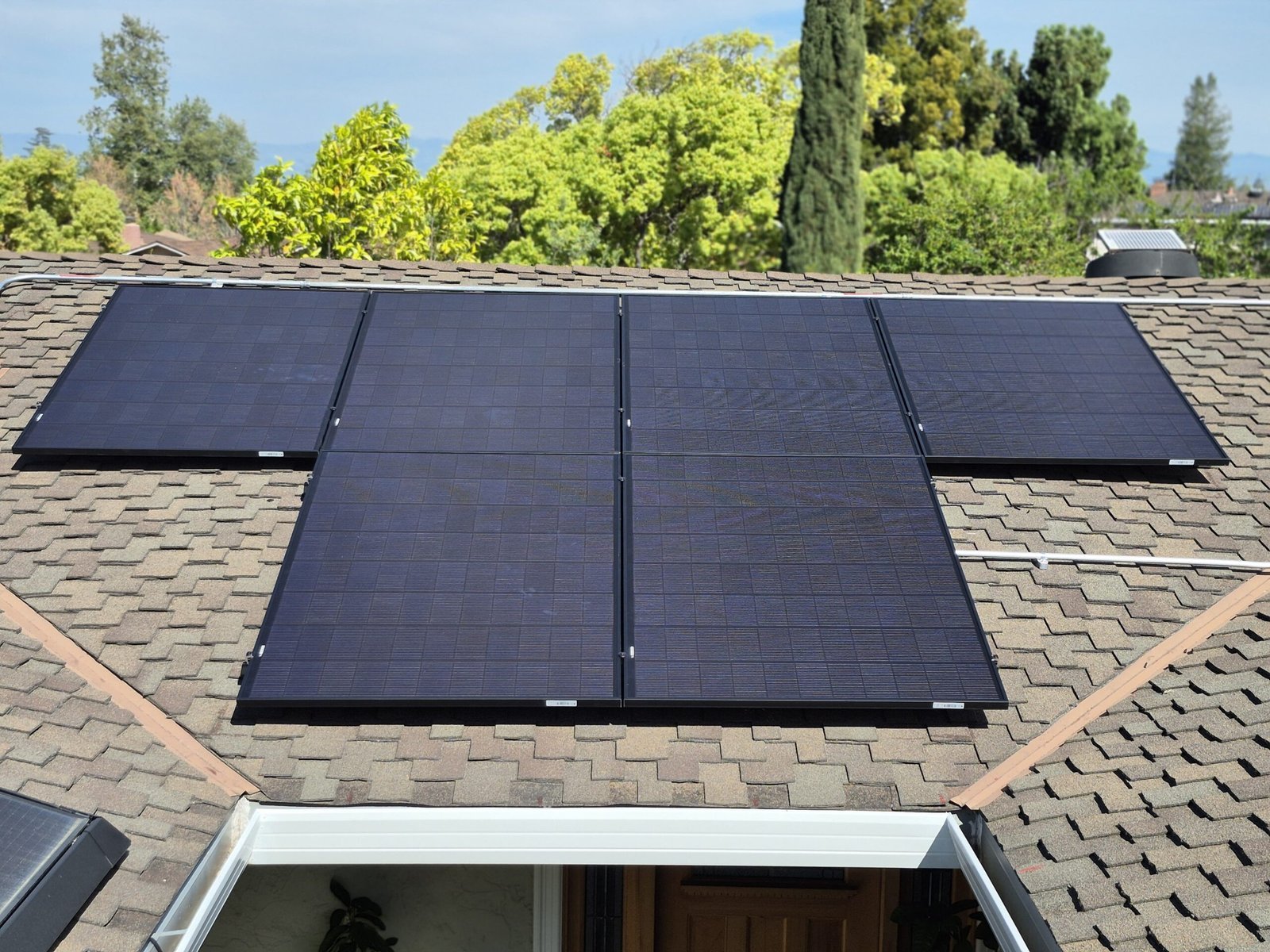 Solar panels arranged around roof vents on a shingle roof surrounded by trees